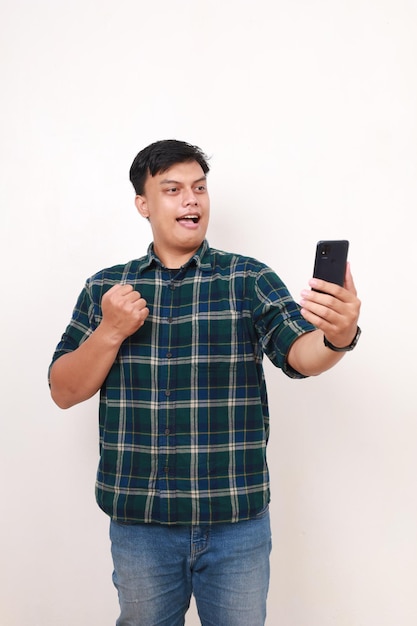 Joven asiático sosteniendo un teléfono celular mientras aprieta la mano con expresión facial feliz