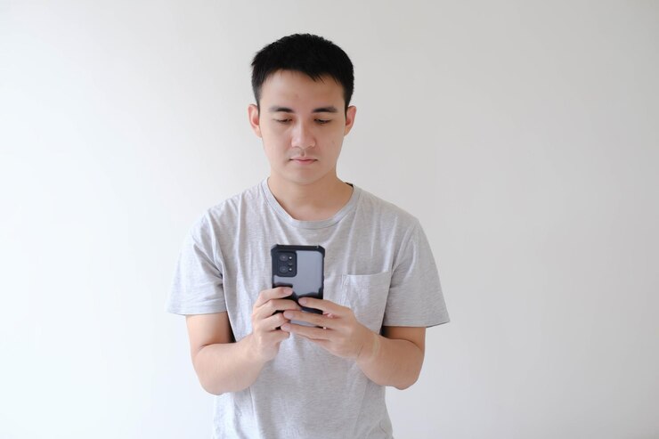 Un joven asiático sostiene y mira un teléfono inteligente