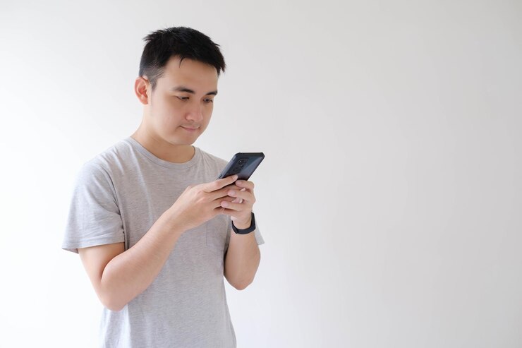 Un joven asiático sostiene y mira un teléfono inteligente