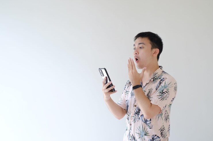 Un joven asiático sostiene un teléfono inteligente con una expresión de asombro