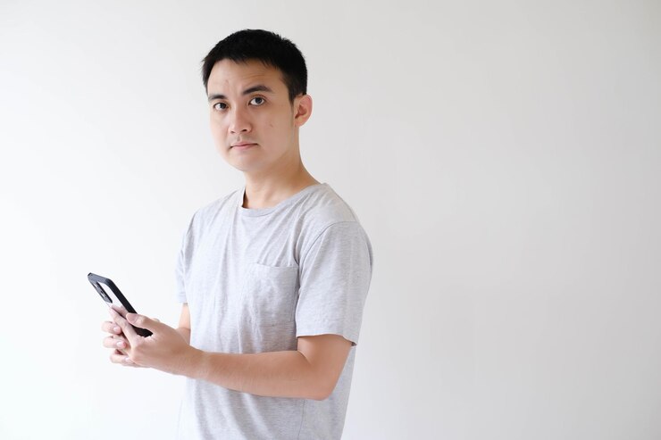 Un joven asiático sostiene un teléfono inteligente y mira la cámara