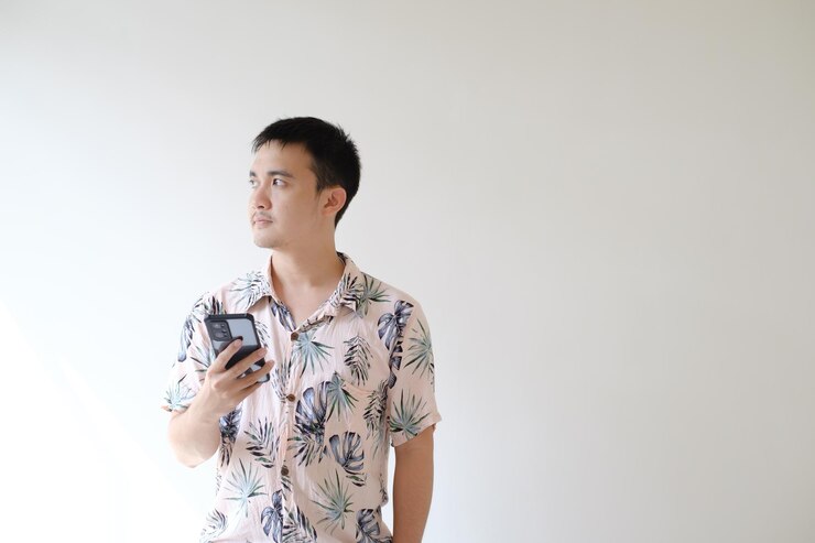 Un joven asiático sostiene un teléfono inteligente y mira hacia el lado izquierdo