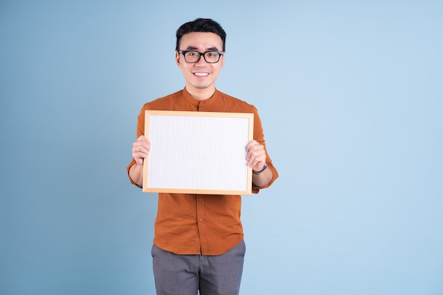 Joven asiático con tablero blanco sobre fondo azul.