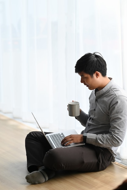 Joven asiático trabajando desde casa en un portátil.