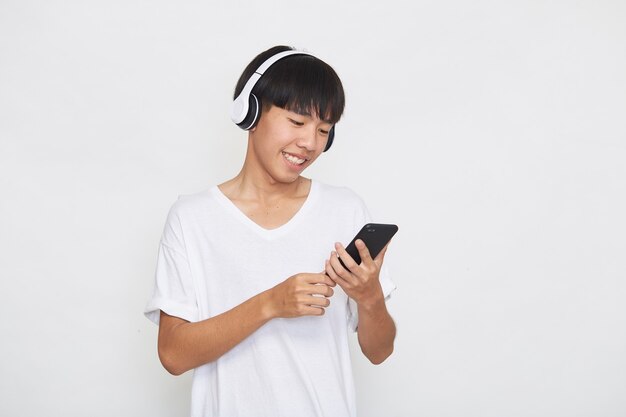 Joven asiático usando audífonos desde un teléfono inteligente en blanco