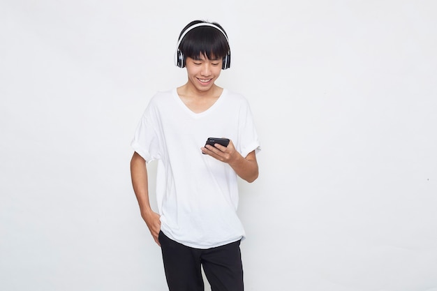 Joven asiático usando audífonos desde un teléfono inteligente en blanco