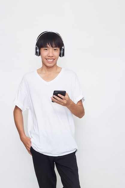 Joven asiático usando audífonos desde un teléfono inteligente en blanco