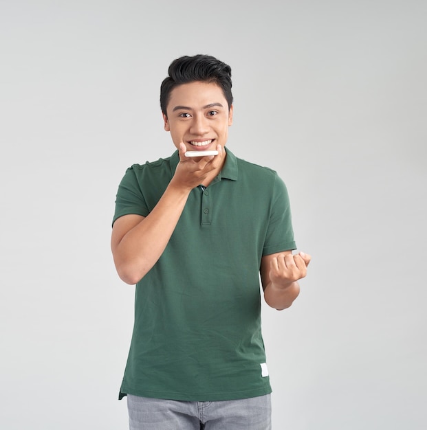 Joven asiático usando una función de reconocimiento de voz de teléfono inteligente aislada en fondo blanco