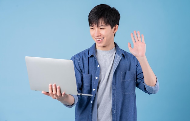 Joven asiático usando una laptop con fondo azul