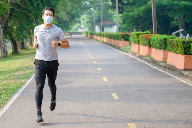 Joven asiático Use una máscara de fitness Correr en el parque Sudoración de un concepto de entrenamiento matutino: use una máscara contra el SARS-Cov-2.