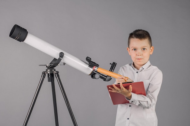 El joven astrónomo mira a través de un telescopio y escribe en la tableta