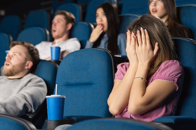 joven asustada escondiendo su rostro detrás de sus manos en una película de terror en el cine