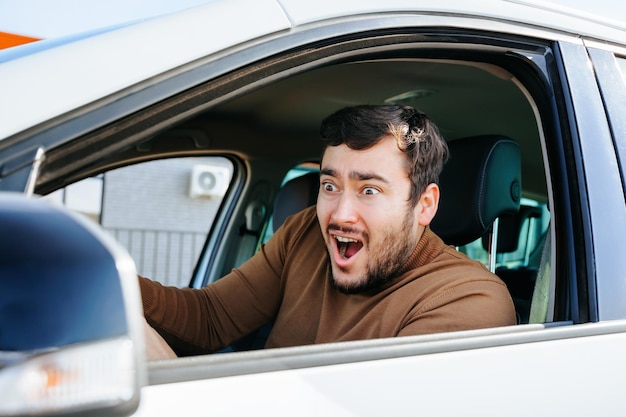 Un joven asustado y sorprendido en un auto detrás del volante grita con ojos saltones y mira hacia adelante