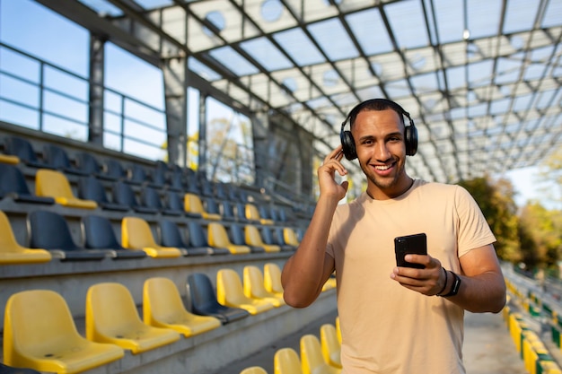 Un joven atleta afroamericano atleta corredor en auriculares se encuentra en el estadio entre