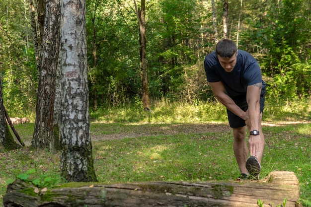 Un joven atleta atlético duradero se está estirando en el bosque al aire libre alrededor del roble del bosque