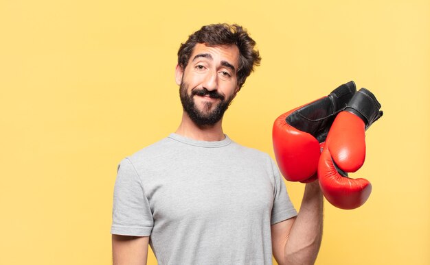 Joven atleta barbudo loco expresión feliz y sosteniendo un guantes de boxeo