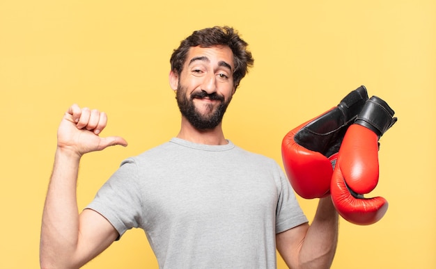 Joven atleta barbudo loco expresión feliz y sosteniendo un guantes de boxeo