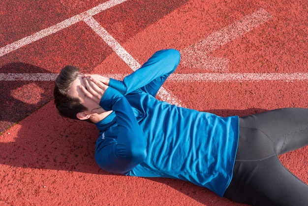 Joven atleta cansado, acostado en la pista de atletismo.