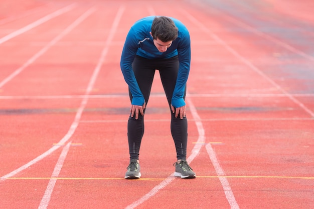 Foto joven atleta cansado, descansando sobre la pista de atletismo.