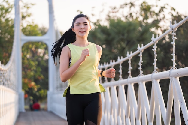 Una joven atleta de corredor de mujer asiática en traje deportivo para correr y hacer ejercicio en el parque de la ciudad por la mañana. Estilo de vida saludable joven mujer asiática deportiva corriendo en el parque tropical. Deporte y recreación