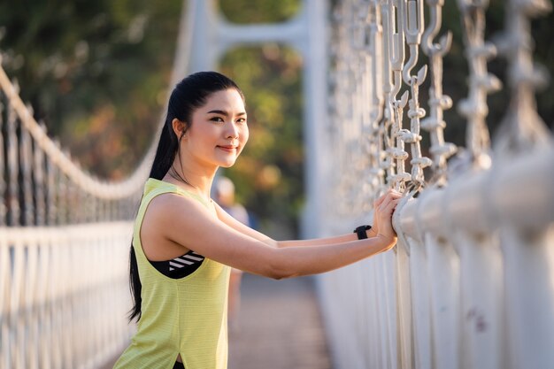 Una joven atleta de corredor de mujer asiática en traje deportivo haciendo estiramientos y calentamiento antes de la sesión de entrenamiento, jogging y entrenamiento físico en el parque de la ciudad por la mañana. Deportes y Recreación