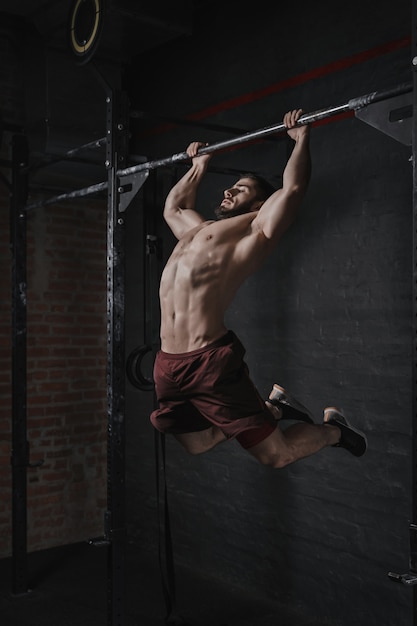 Joven atleta crossfit haciendo dominadas en el gimnasio. Hombre guapo haciendo entrenamiento funcional. Practicando calistenia.