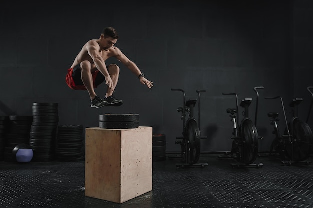 Joven atleta de crossfit haciendo ejercicio de salto de caja en el gimnasio