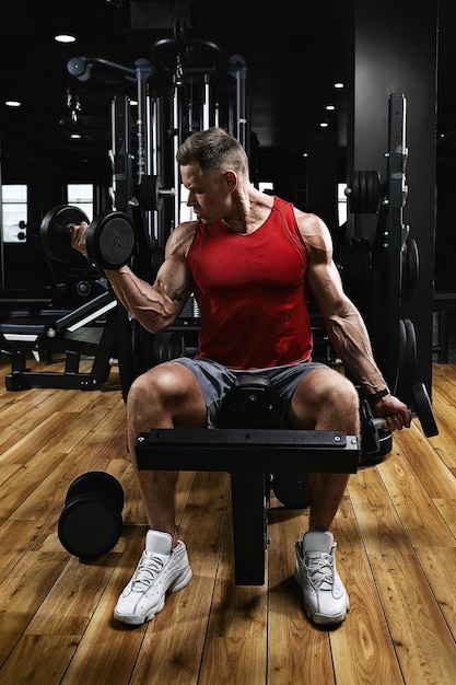 Joven atleta deportivo modelo de fitness en el gimnasio sacude sus bíceps con pesas. Motivación deportiva, bajo perfil, alto contraste. El concepto de un estilo de vida saludable, movimiento de vida, espacio de copia.