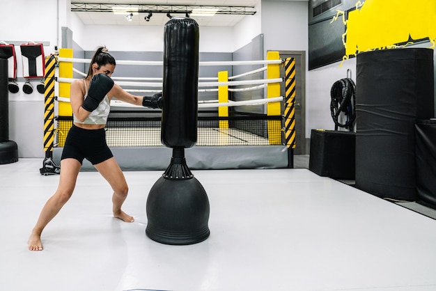 Un joven atleta descalzo practicando golpeando la bolsa de entrenamiento en el gimnasio.