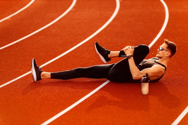 Joven atleta descansando después de correr en el estadio en verano