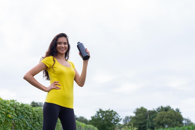 Joven atleta femenina étnica bebiendo agua después de entrenar en la naturaleza