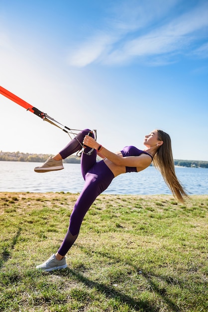 Joven atleta femenina haciendo ejercicios matutinos entrenando con correas de fitness trx en el parque. Concepto de estilo de vida y entrenamiento saludable