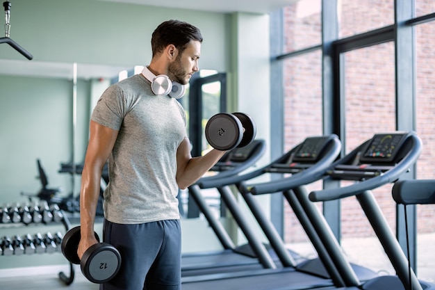 Joven atleta haciendo ejercicio con pesas de mano en el club de salud