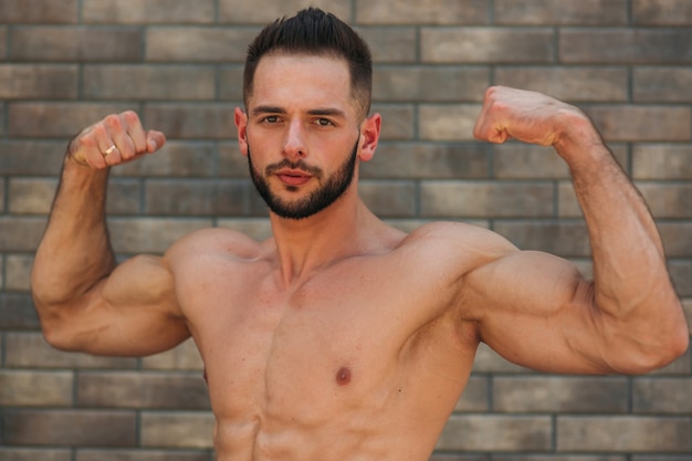 Joven atleta posando con un torso para fotografía sobre un fondo de pared de ladrillo. Culturista, atleta con músculos bombeados, rescate de senos y brazos