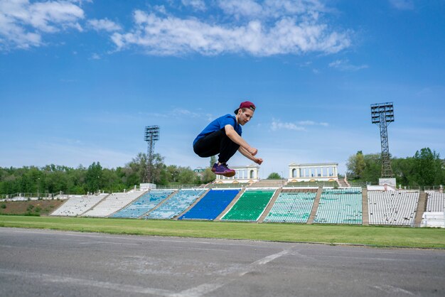 Joven atleta practica salto alto salto en el aire en el estadio en días de verano