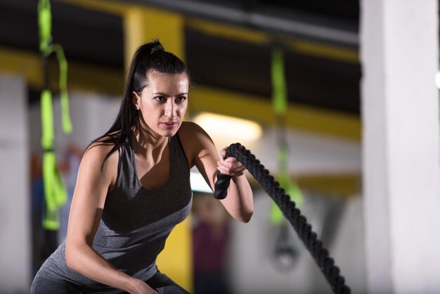 Una joven atleta que trabaja en un gimnasio de entrenamiento funcional haciendo ejercicios de cuerdas de batalla como parte del entrenamiento de fitness cruzado