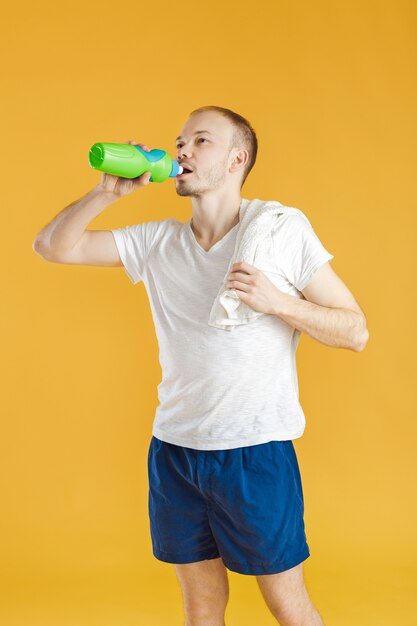 Joven atleta con una toalla beber agua después de un entrenamiento en un amarillo