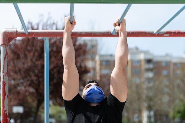 Joven atleta trabajando bíceps en un gimnasio al aire libre haciendo ejercicios de entrenamiento callejero