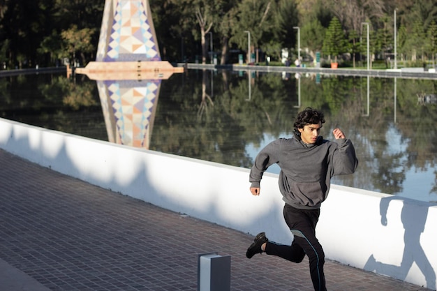 Joven atleta trotando en el parque al aire libre entre la naturaleza junto al lago por la mañana