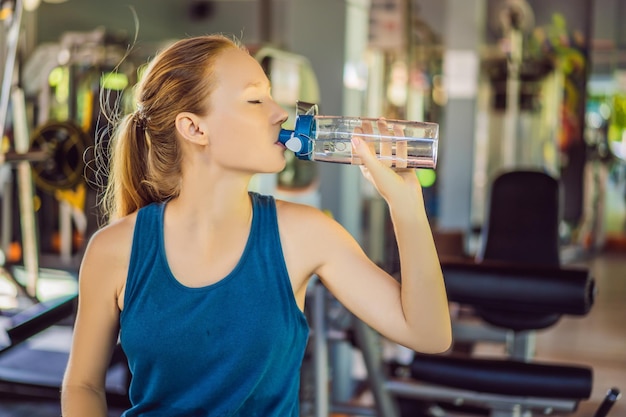 Joven atlética agua potable en el gimnasio