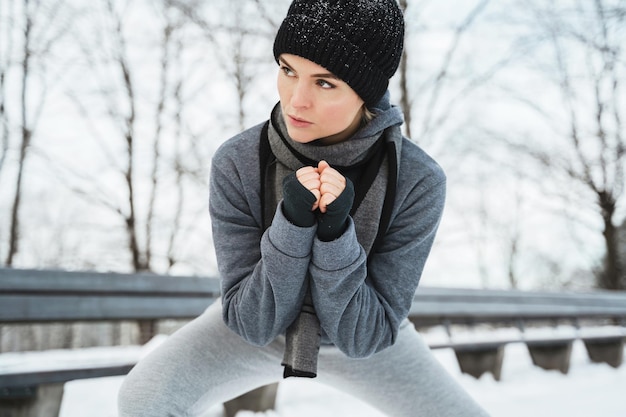 Joven atlética calentándose antes de su entrenamiento de jogging durante el día de nieve de invierno en un parque de la ciudad