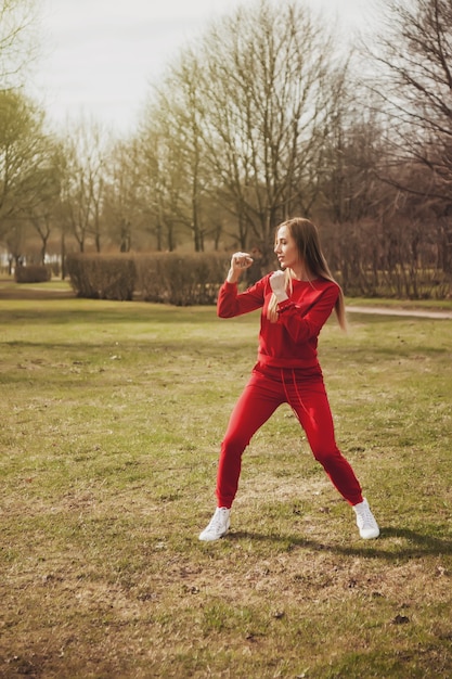 Joven atlética se dedica a ejercicios deportivos en el parque en primavera, al aire libre. Mujer profesional en traje rojo en la sesión de formación. Concepto de estilo de vida saludable. Copie el espacio para el sitio