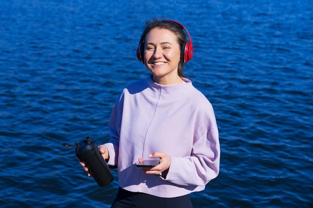 Una joven atlética escucha música y bebe agua durante los descansos del entrenamiento al aire libre
