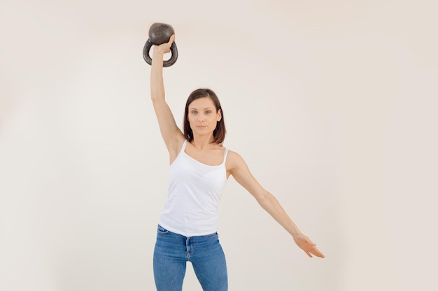 Foto joven atlética levantando pesas rusas y bajando el brazo fondo blanco manteniéndose en forma por stre