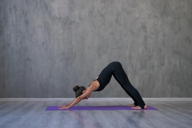Joven atlética practica yoga boca abajo aislado en la pared gris