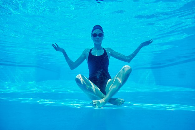 Foto joven atlética sentada en postura de loto bajo el agua en la piscina