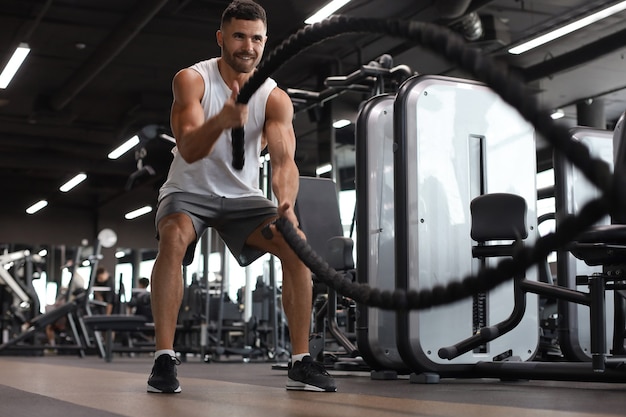 Joven atlético con cuerda de batalla haciendo ejercicio en el gimnasio de entrenamiento funcional.