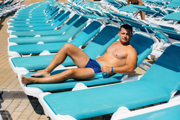 Un joven atlético está sonriendo felizmente y tomando el sol en una tumbona en un día soleado. Felices vacaciones vacaciones. Vacaciones de verano y turismo.