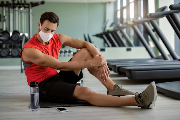 Joven atlético con mascarilla tomando un descanso mientras entrena en un gimnasio