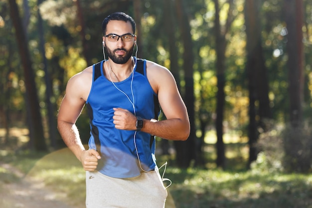 Foto joven atlético multicultural barbudo con gafas deportivas corriendo y escuchando su música favorita estilo de vida saludable y concepto de personas